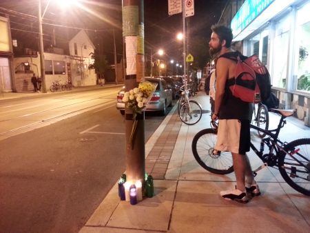 A steady stream of cyclists and other passerby stop to observe the roadside memorial.