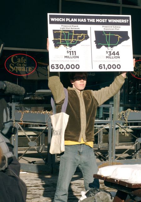 A rally organizer holds a sign displaying the differences between Transit City and Mayor Rob Ford's transit plan on Sunday, Jan. 9, 2011 (Thom Leigh for TMC)